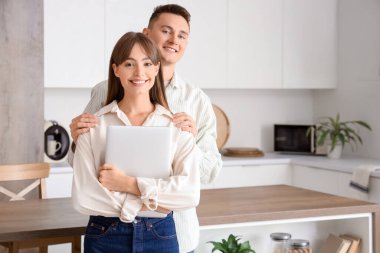 Dizüstü bilgisayarlı genç çift mutfakta sarılıyor.