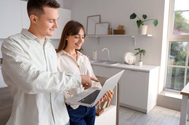 Genç çift mutfakta dizüstü bilgisayar kullanıyor.