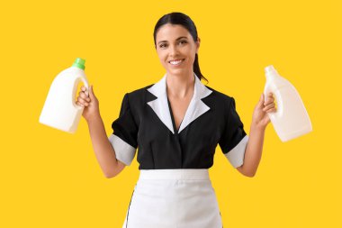 Sarı arka planda deterjanları olan genç oda hizmetçisi.