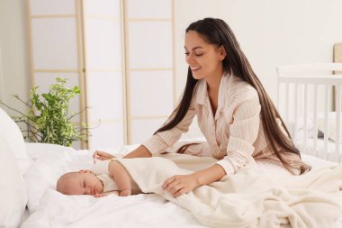 Anne yatak odasında uyuyan bebeğini yumuşak bir battaniyeyle örtüyor.
