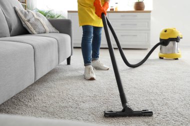 Evde elektrikli süpürge ve temizlik halısı olan genç bir kadın.