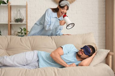 Megafonlu mutlu genç bir kadın ve pijamalı erkek arkadaşı evdeki kanepede uyuyor.