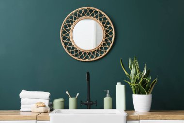 Banyoda yeşil duvarın yanında banyo aksesuarları ve bitkiler var.