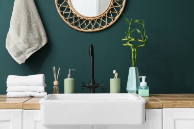 Lavabo ve banyo aksesuarları banyodaki yeşil duvarın yanında.