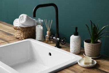 Banyoda yeşil duvarın yanındaki ahşap masada farklı banyo aksesuarları.