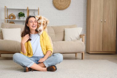 Avustralya çoban köpeği olan genç bir kadın evde yerde oturuyor.