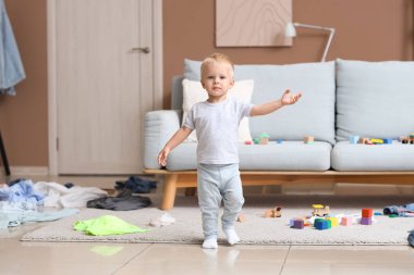 Dağınık odada yürüyen tatlı bir erkek bebek.