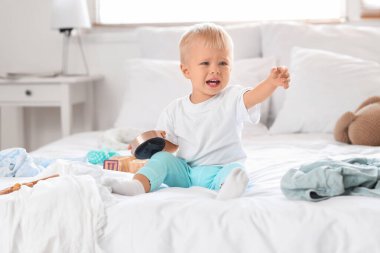 Crying baby boy with alarm clock sitting in messy bedroom clipart