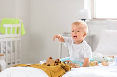 Crying baby boy with toys in messy bedroom clipart