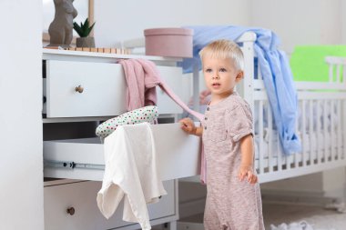 Yaramaz çocuk, dağınık yatak odasında elbiseleriyle çekmece açıyor.