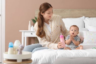 Bir şişe sütle annesi ve küçük bebeği yatak odasında oturuyor.