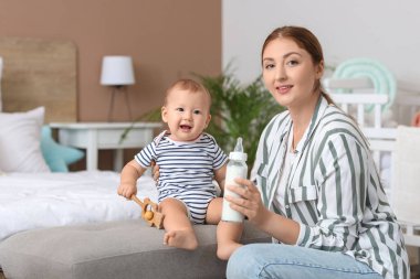 Bir şişe sütle annesi ve küçük bebeği yatak odasında.