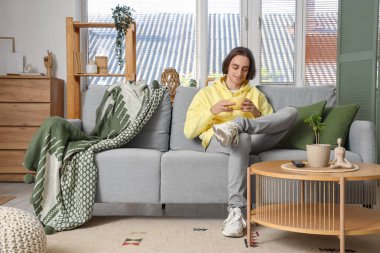 Evdeki kanepede oturan bir fincan çayla genç adam.