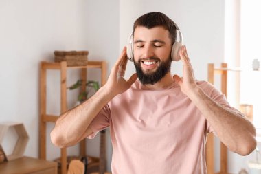 Kulaklıklı genç sakallı adam evde müzik dinliyor.