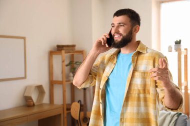 Evde cep telefonuyla konuşan genç sakallı adam.