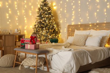 Yatak odasının içinde Noel ağacı, hediyeler ve parlayan ışıklar var.