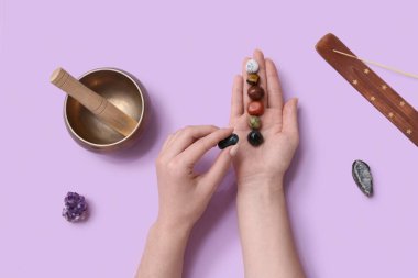 Chakra taşları, aroma çubuğu ve eflatun kaplamalı Tibet kâsesi olan bir kadın.