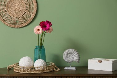 Vazodaki güzel gerberalar, hasır tepsi ve kutu yeşil duvarın yanındaki odada.