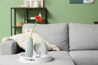 Oturma odasındaki kanepede üzerinde Gerbera çiçeği ve heykel olan vazo.