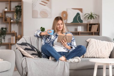 Evdeki kanepede çay fincanı okuyan genç bir kadın.