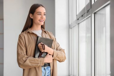 Kutsal kitabı ve dua boncukları olan genç bir kadın.