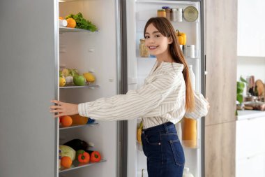 Genç bir kadın mutfakta buzdolabı açıyor.
