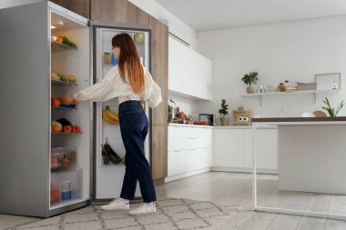 Genç bir kadın mutfaktaki buzdolabına meyve suyu koyuyor.