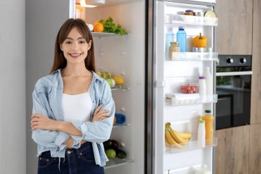 Mutfaktaki açık buzdolabının yanında genç bir kadın.