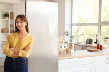 Genç bayan mutfaktaki modern buzdolabının yanında.