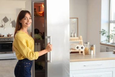 Genç bir kadın mutfakta buzdolabı açıyor.