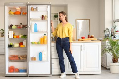 Mutfakta bir sürü ürünü olan açık buzdolabının yanındaki genç kadın.