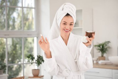 Banyoda hindistancevizi ve krema dolu bir kavanozla güzel, genç ve mutlu bir kadın.