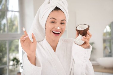 Banyoda hindistancevizi ve krema dolu bir kavanozla güzel, genç ve mutlu bir kadın.