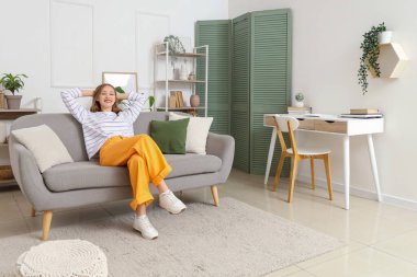 Evdeki gri kanepede dinlenen genç kadın.