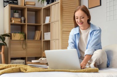 Yatak odasında dizüstü bilgisayar kullanan genç kadın.