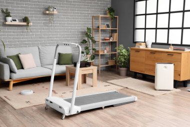 Oturma odasının içinde kanepe, koşu bandı ve aletler var.