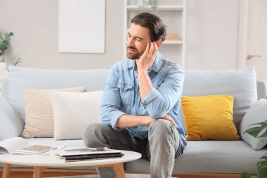 Evdeki kanepede kulak ağrısından muzdarip yakışıklı genç adam.