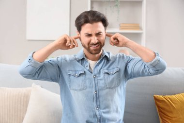 Evdeki kanepede kulaklarını kapatmakta zorlanan genç bir adam.