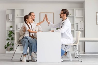 Erkek çocuk doktoru klinikte kız ve anneye beşlik çakıyor.
