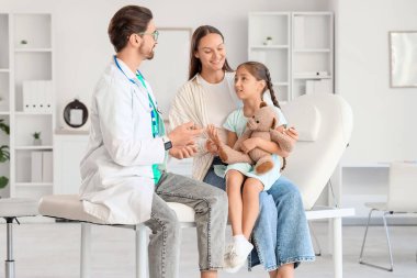 Oyuncak ayıyla tatlı bir kız ve annesi klinikteki çocuk doktorunu ziyaret ediyor.