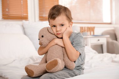 Yatak odasında kulak ağrısından muzdarip oyuncak ayılı küçük çocuk.