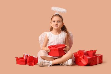 Aşk tanrısı gibi giyinmiş, kahverengi arka planda hediye kutuları olan sevimli küçük bir kız. Sevgililer Günü kutlaması