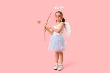 Aşk tanrısı gibi giyinmiş, oklu ve pembe arka planda eğilmiş şirin küçük bir kız. Sevgililer Günü kutlaması