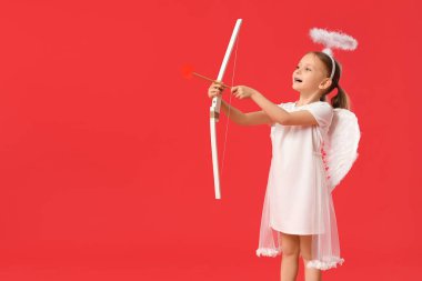 Oklu aşk tanrısı gibi giyinmiş ve kırmızı arka planda eğilmiş şirin küçük bir kız. Sevgililer Günü kutlaması