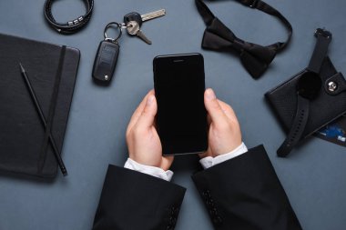 Cep telefonlu erkek eller ve gri arka planda şık aksesuarlar.