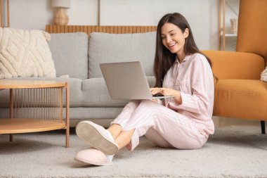 Çizgili pijamalı genç bir kadın evde dizüstü bilgisayarla çalışıyor.