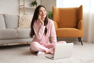 Evde cep telefonuyla konuşan pembe pijamalı, serbest çalışan bir kadın.