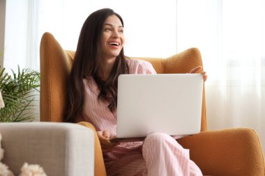 Evde dizüstü bilgisayarla çalışan pembe pijamalı serbest çalışan bir kadın.