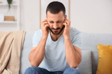 Evdeki kanepede kulaklarını kapatmakta zorlanan genç bir adam.