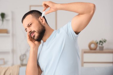 Evde kulağına damla damlatan işitme sorunu olan genç bir adam.